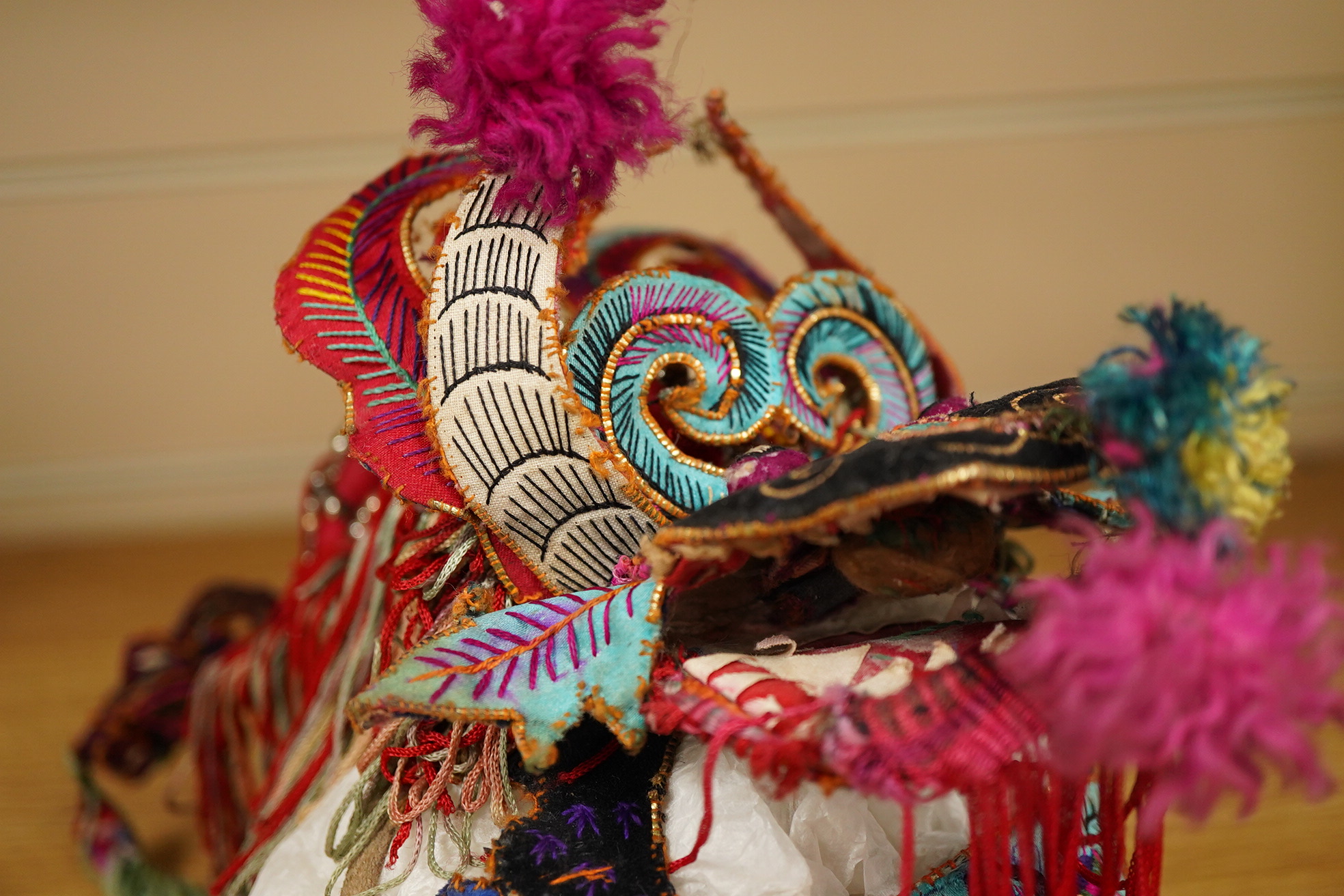 A decorative Chinese child’s festival ‘dragon’ hat, decorated with embroidered panels, tasselling and pom-poms with an elaborate dragon face and head dress. 20cm high. Condition - tasselling is missing around the dragons